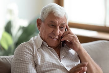 Smiling older man speaking on the phone at home, representing how EMMA by QuantumLoopAI helps bridge the digital divide in healthcare by making AI technology accessible and inclusive for all NHS patients.