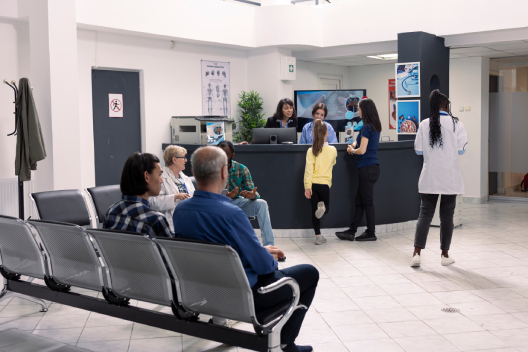 Busy GP surgery reception with patients waiting and staff assisting at the front desk, representing how EMMA by QuantumLoopAI reduces call queues and improves patient flow across NHS practices.