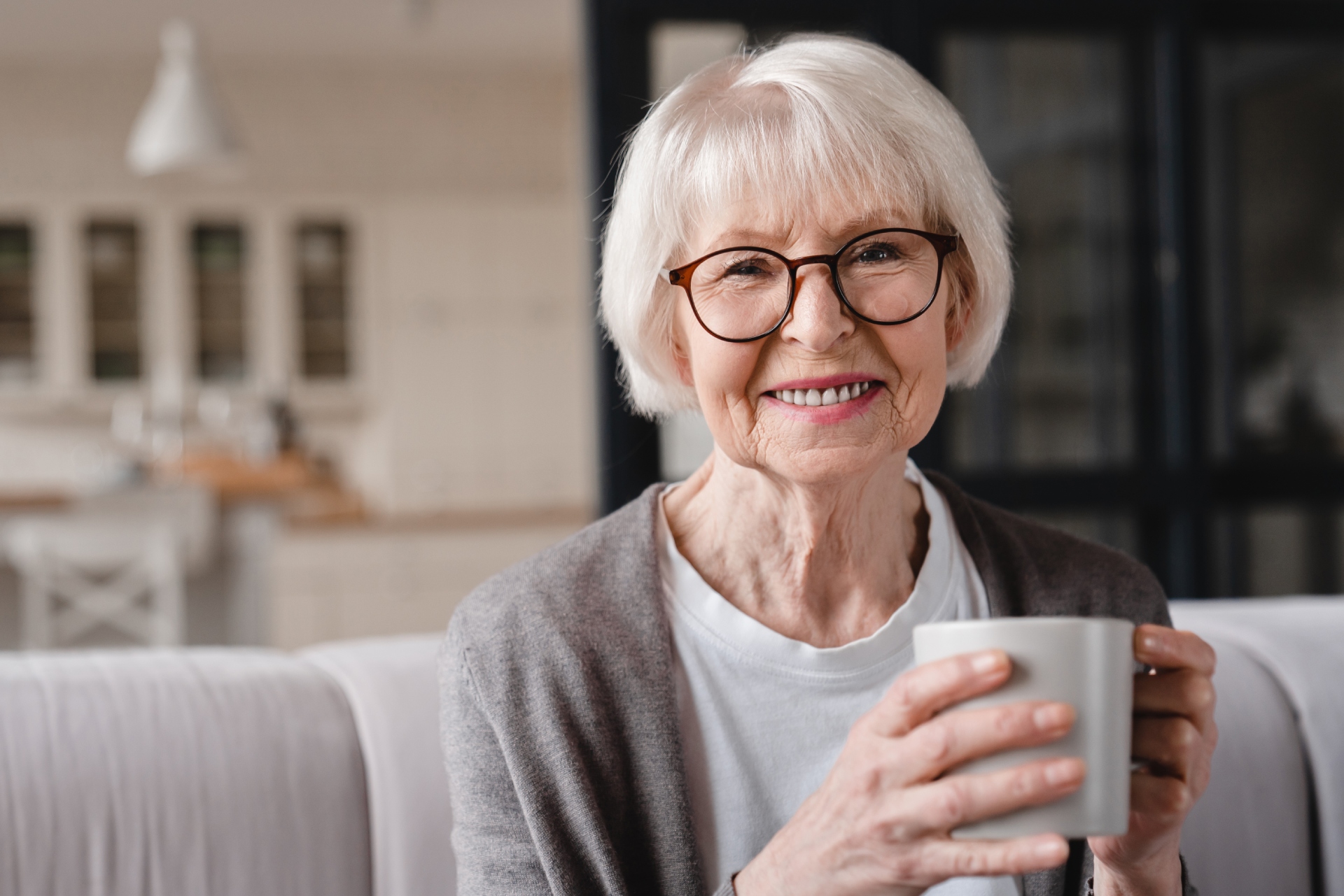 Older female patient smiling with a cup of tea, representing easy access to care through EMMA by QuantumLoopAI — the AI reception for NHS GP surgeries.