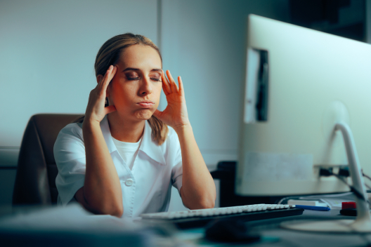 Stressed GP receptionist sitting at a computer with her hands on her head, representing the burnout and pressure faced by primary care staff before solutions like EMMA by QuantumLoopAI improve retention and job satisfaction.