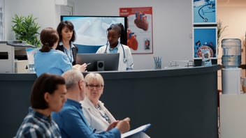 P surgery reception with medical staff supporting patients and managing appointments, representing how EMMA by QuantumLoopAI streamlines communication and reduces call volumes across NHS practices.